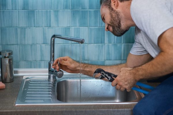 Fix a leak. Close up shot of professional repairman using pipe wrench while examining and fixing faucet in the kitchen. Repair service and plumbing concept. Horizontal shot